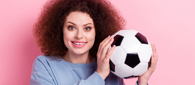 Mulher sorrindo e segurando bola de futebol